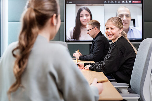 Mehrere Personen mit einem Online-Meeting im Hintergrund