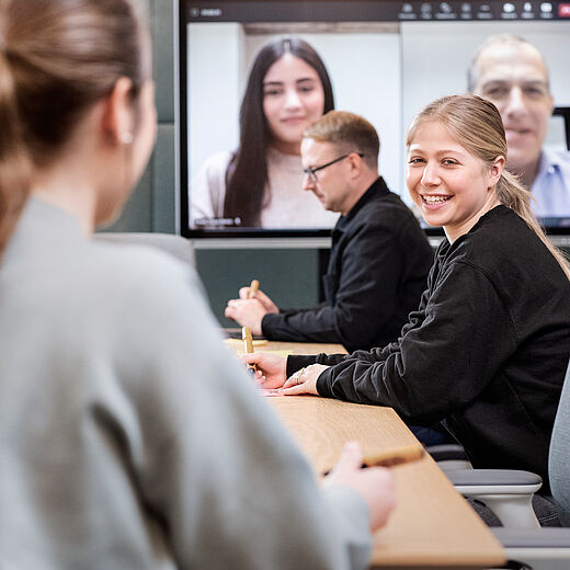 Mehrere Personen mit einem Online-Meeting im Hintergrund
