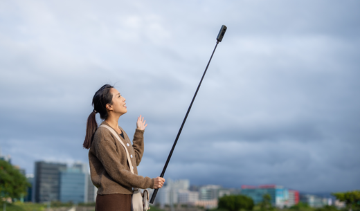 Frau mit Selfie-Stick vor bewölktem Himmel draußen.