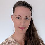 Porträt einer Frau mit langen, glatten Haaren und einem leichten Lächeln. Sie trägt ein gestreiftes Oberteil und schaut direkt in die Kamera. Der Hintergrund ist neutral und hell.